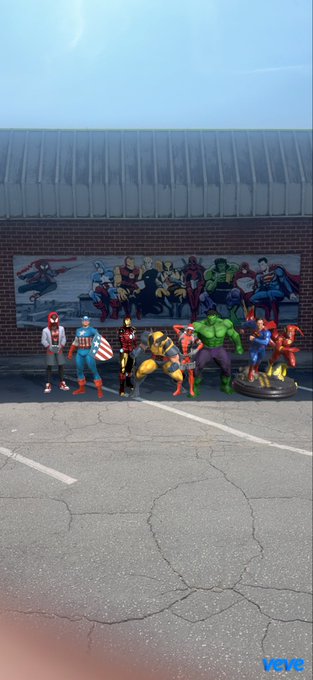 A lineup of various Marvel action figures including Spider-Man, Captain America, Iron Man, Wolverine, Hulk, and others stands posed in a parking lot in front of a mural depicting the same characters. The "VEVE" watermark is visible in the bottom right, tying the image to the Veve digital collectibles platform mentioned in the caption.