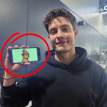 A man in a black hoodie holding up a smartphone displaying a small animated cartoon character, with the phone screen circled in red.