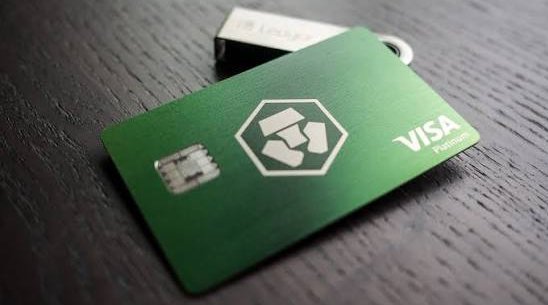 A green Visa Platinum debit card branded with the Crypto.com logo resting on a dark wooden surface.