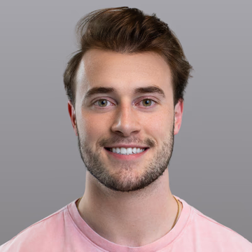 The image features a man with brown hair wearing a pink shirt, smiling at the camera. The caption below the photo reads "JOE CONSORTI: Bitcoin is the only emergent financial technology that works as a neutral settlement layer in an increasingly trustless and fractured world order." This statement suggests that the man's smile could be related to or inspired by the concept of Bitcoin, which has been gaining popularity due to its potential for anonymity and decentralization.