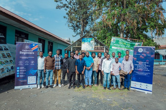 A group photo of attendees at a 'Cardano for Beginners' event, standing outdoors in front of informational banners in French.