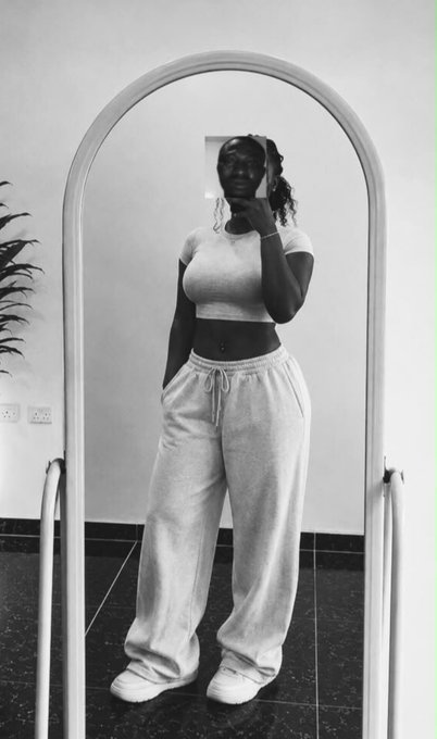 A black-and-white mirror selfie of a woman wearing a gray crop top and matching sweatpants, posing confidently while taking the photo with her phone. The simple, stylish "fit pic" complements the upbeat, fresh-start vibe of the new month greeting and $RIVER token mention.