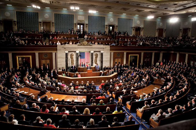 The image shows a large room filled with people sitting in wooden chairs facing each other at a long table. The scene appears to be taking place inside a U.S. House of Representatives, where a group of people are engaged in a discussion or debate about a specific topic. The focus on the image is on the people and their actions rather than any specific details related to the post.