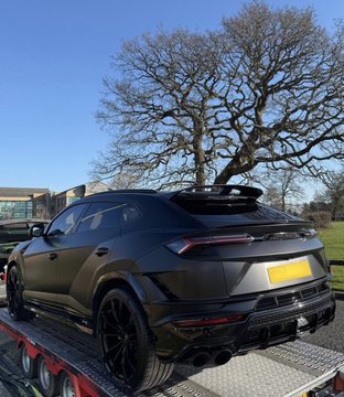 A matte black Lamborghini Urus SUV is loaded on a flatbed tow truck, with its yellow UK license plate visible. The image illustrates the poster's achievement of getting a luxury vehicle "fully paid for" thanks to their crypto/Web3 success.