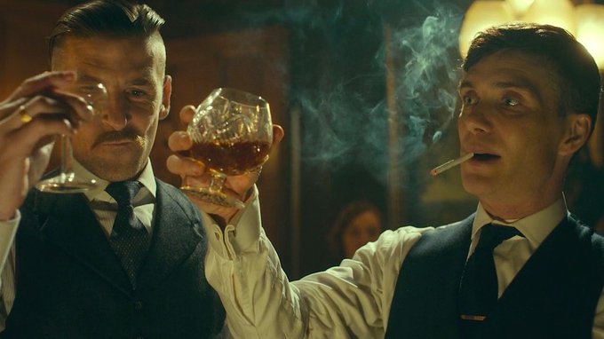 Two well-dressed men in vests and ties raise crystal glasses in a toast, one holding a whiskey glass while the other smokes a cigarette with smoke swirling dramatically around him, evoking the high-stakes, glamorous danger of a $75,000 Bitcoin transaction in a Prohibition-era speakeasy setting.