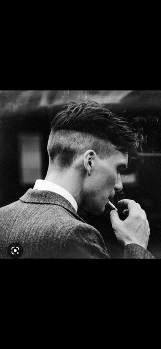 A black and white photo of a man in a tweed suit smoking a cigarette, showing a profile view with a modern haircut.