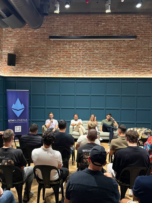 A panel discussion at an Ethereum Slovenia event, with four speakers seated on a couch in front of an audience in a brick-walled venue.