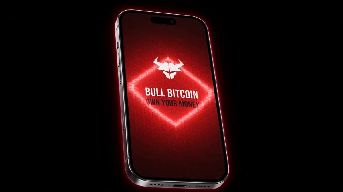 The image features a smartphone with a red screen displaying an advertisement for Bitcoin. The phone's screen shows a bulldog logo, which is associated with Bitcoin. The text "Bull Bitcoin" is written above the bulldog logo, indicating that the phone supports Bitcoin transactions. The phone appears to be turned on and is placed against a black background.
