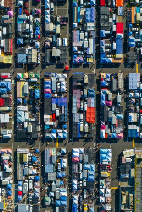 An aerial view of a densely packed outdoor market or festival with rows of colorful tents and stalls.
