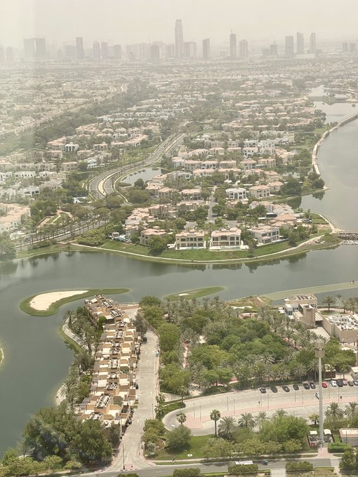 An aerial view of a coastal residential area with winding roads, water canals, and a city skyline in the background.