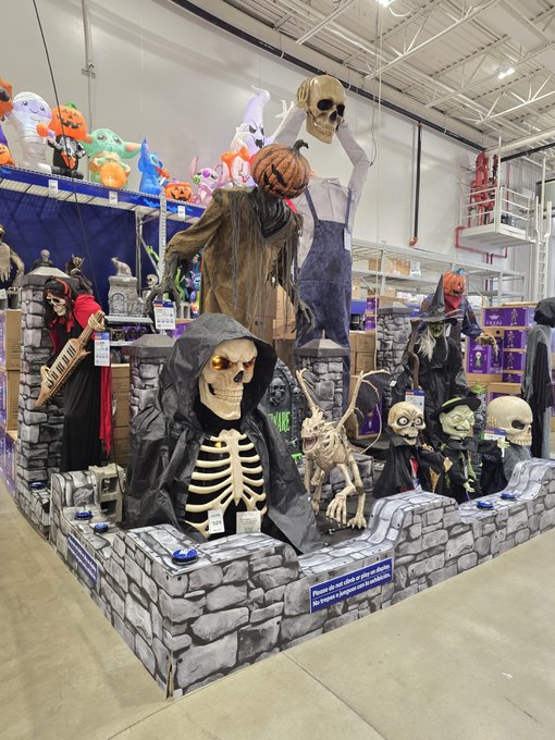 A Halloween display in a store featuring various spooky decorations including skeletons, grim reapers, ghosts, and pumpkins arranged on faux stone walls.
