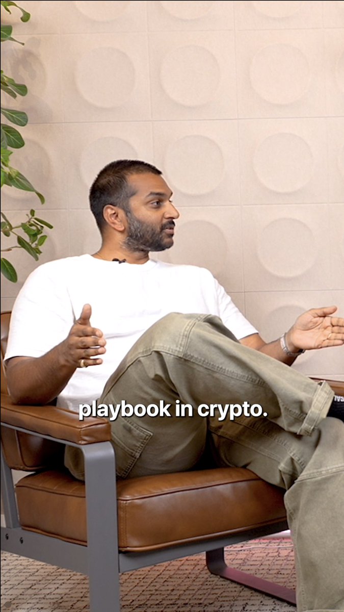 A man in a white t-shirt and olive green pants sits in a brown leather chair, gesturing with both hands while speaking. The caption "playbook in crypto." appears at the bottom, illustrating the post's discussion about how success in crypto can't rely on traditional Web2 playbooks.