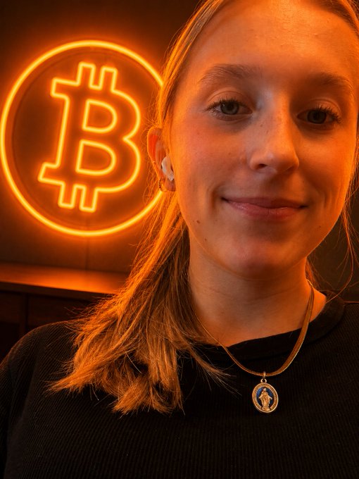 A woman smiles in front of an illuminated orange Bitcoin logo, visually echoing the "orange pill" metaphor of spreading crypto awareness. Her warm expression reflects acceptance of the post's message—that conviction, like Bitcoin adoption, can't be forced onto others.