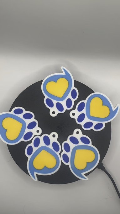 Five die-cut stickers featuring a blue paw print design with a yellow heart in the center are arranged in a circle on a black surface.