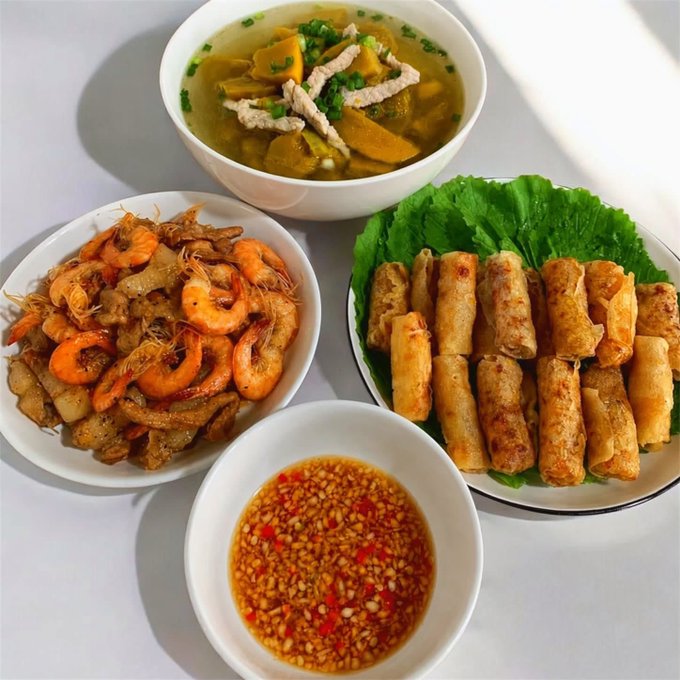 A spread of Vietnamese dishes including a bowl of soup with pork, a plate of stir-fried shrimp and pork belly, fried spring rolls on lettuce leaves, and a small bowl of chili dipping sauce.