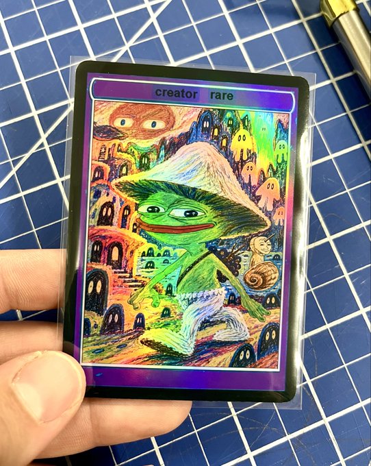 A hand holds a holographic trading card featuring a Pepe the Frog character in a pointillist art style, labeled 'creator' and 'rare' at the top.