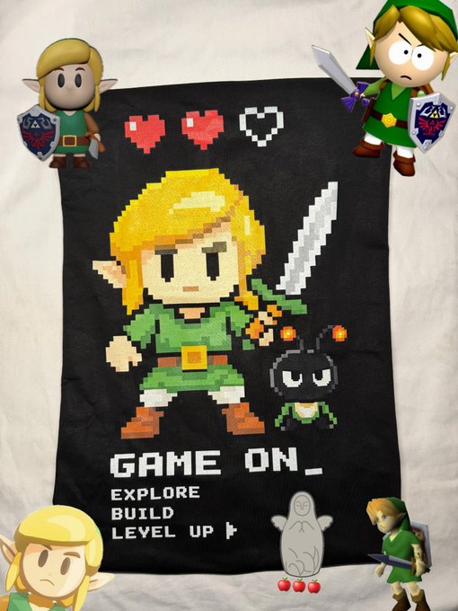 A black graphic t-shirt featuring a pixel art design of Link from The Legend of Zelda, accompanied by the text 'GAME ON_ EXPLORE BUILD LEVEL UP' and pixelated hearts.