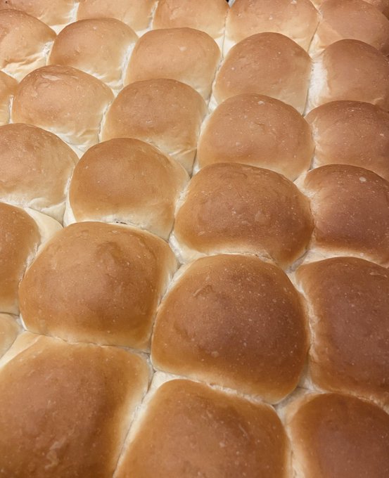 A close-up photograph of rows of golden-brown dinner rolls arranged tightly together on a baking sheet.