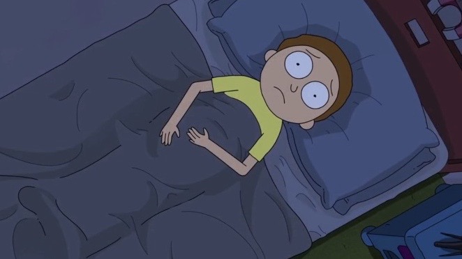 A scene from the animated show Rick and Morty showing Morty Smith lying in bed at night with a worried, wide-eyed expression, wearing a yellow shirt.