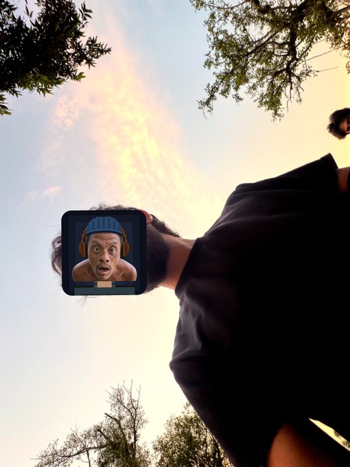A low-angle shot of a person outdoors at sunset with a digital avatar (resembling a shocked emoji with a beanie and headphones) superimposed over their face.