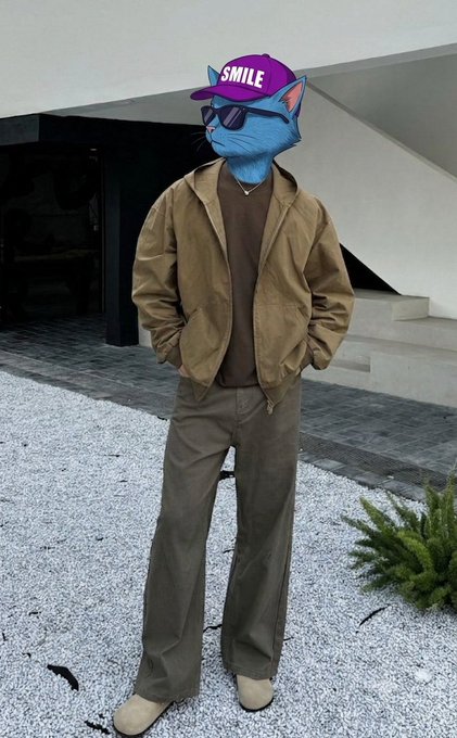 A person with an edited blue cat face wearing a pink "SMILE" cap, sunglasses, brown jacket, and tan pants stands in a courtyard, perfectly matching the upbeat "good morning X, it's a new day to try again" vibe with their fashionable, positive-aesthetic outfit.