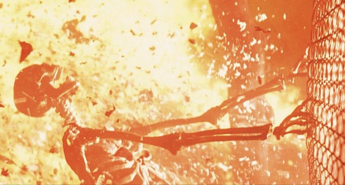 An action scene shows a skeleton in a burning environment as an explosion erupts, with intense orange flames filling the frame.