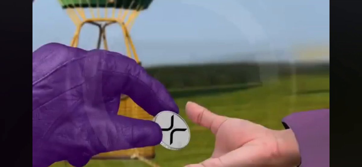 The image features a purple glove being held by someone's hand with an object inside their other hand. The person wearing the glove appears to be handing over something, possibly a coin or a keychain, while the other person receives it. The background of the image is blurred and does not provide any additional information about what they are handing over.