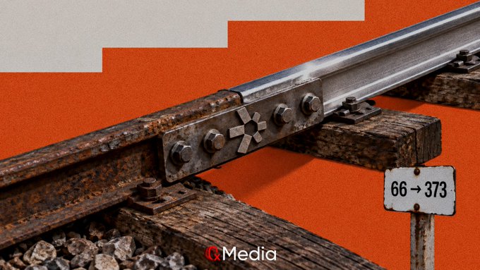 A close-up of a rusted train track joint on a wooden railroad tie, with a white sign reading '66 → 373' and 'Q Media' watermarked at the bottom.