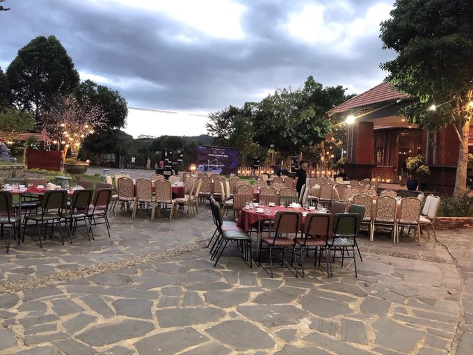 An outdoor evening event setup with round tables covered in red tablecloths and numerous chairs arranged on a stone-paved courtyard at dusk. The scene matches the post's relaxed social vibe of weekend drinks and friendly conversation, while the mention of "alpha" market opportunities and tagging @useTria suggests a financial meetup or networking gathering is being organized.