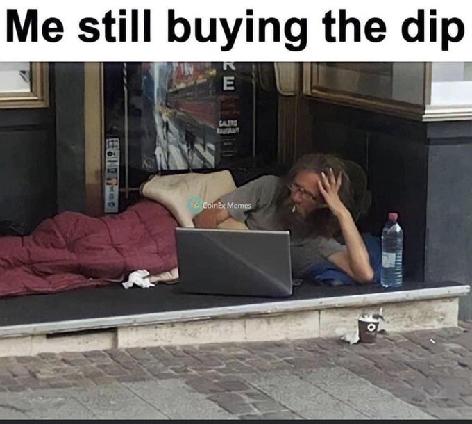 A 'CoinExMemes' meme captioned 'Me still buying the dip' shows a disheveled bearded man lying on the street with a laptop, water bottle, and shopping cart, watching his crypto portfolio.