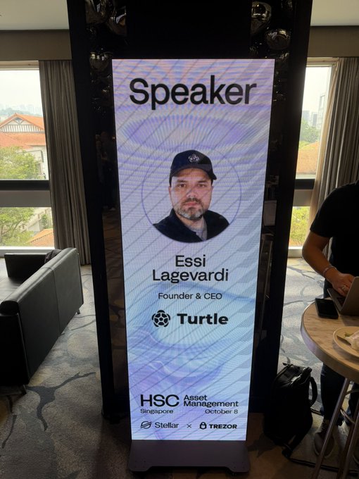 A digital display identifies "Speaker: Essi Lagevardi, Founder & CEO, Turtle" at the HSC Asset Management Singapore summit on October 8, alongside Stellar and Trezor sponsorship logos—visually promoting Turtle's leadership role at the event described in the post about connecting allocators with issuers needing capital.
