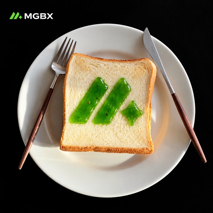 A slice of bread sits on a white plate with a fork and knife, topped with green jelly shaped like the letter 'M' and a star, with 'MGBX' written in the top left corner.