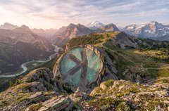 A scenic mountain landscape featuring turquoise alpine lakes nestled among rugged, sunlit peaks under a soft sky.