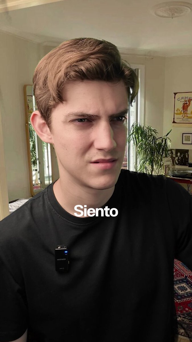 The image features a young man wearing a black shirt, with his face partially visible as he looks at something off-camera. The background includes a mirror reflecting the room's interior, including a potted plant and a couch. There are also some books scattered around the scene. The photo seems to be related to Bitcoin or cryptocurrency, as indicated by the caption "Why do I feel like life is getting more and more expensive? #Bitcoin".