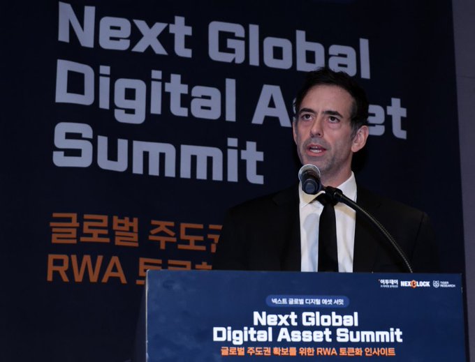 The image features a man standing at a podium, giving a speech or presentation. The setting appears to be an event related to digital asset trading, as indicated by the presence of a banner that reads "Next Global Digital Asset Summit". The speaker is wearing a suit and tie, suggesting a formal occasion for his address. The text in the image also mentions the RWA network's coverage about @CantonNetwork in Korea on October 1st, which could be related to the event or the digital asset trading industry as a whole.