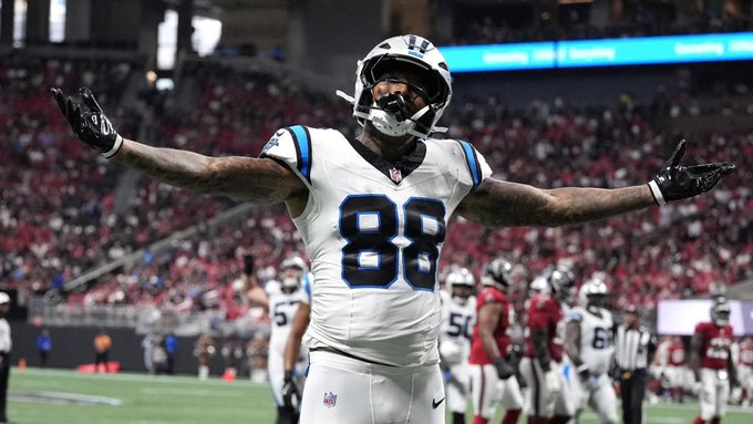 Carolina Panthers tight end Darren Waller, wearing jersey #88, celebrates with arms outstretched in his white and blue away uniform after scoring a touchdown against the Atlanta Falcons, connecting with the giveaway post's focus on his first-TD performance.