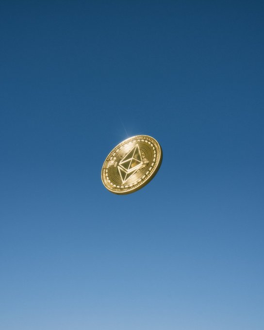 A gold Ethereum coin spinning against a clear blue sky.
