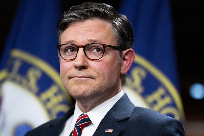 A man wearing dark-rimmed glasses, a dark suit, and a striped red tie stands in front of a blue flag bearing a gold seal, likely a House Speaker's image, suggesting a formal press or political setting. The accompanying "Read the full story:" prompt indicates the photo is used as a lead image to invite readers into an article, with the man's serious expression conveying the gravity of the news being discussed.