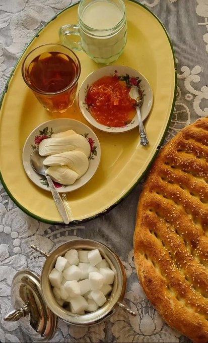 A yellow tray holds a glass of milk, tea, butter, orange jam, and sugar cubes alongside a sesame-topped flatbread, presented as a cozy traditional breakfast spread that complements the cheerful "Happy Wednesday" post.