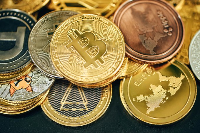 A pile of physical cryptocurrency tokens featuring Bitcoin's ₿ logo, Monero, and Ripple coins. The image of physical crypto coins relates to the post's call for AI developers to help secure cryptocurrency and financial infrastructure like Bitcoin.