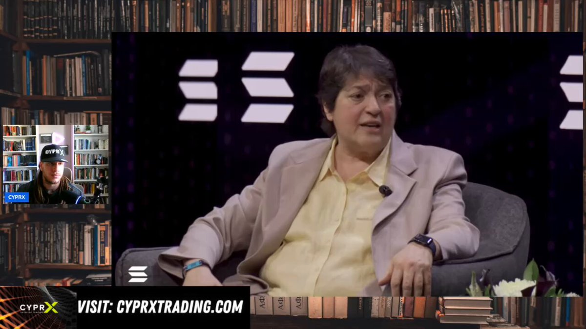 The image shows a woman sitting in an office chair, wearing a suit jacket and talking into a microphone during a video call with another person. The background of the image features bookshelves filled with various books, suggesting that they are taking place in a professional setting or a workspace. The caption at the bottom of the image reads "HOLY SH*T SHARE THIS VIDEO BIGGEST CONFIRMATION FROM THE DTCC TO DATE! $CC XLM ... FOR NOW BUT THERE WILL BE MANY". This indicates that the woman is sharing important information with her colleague, possibly discussing a significant event or news related to their work.