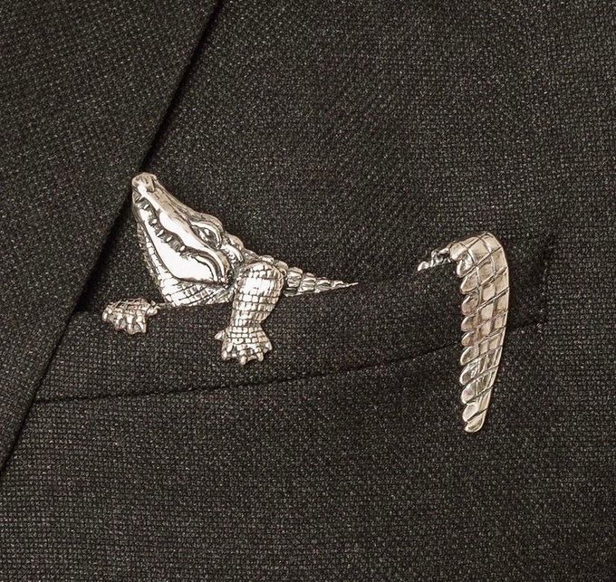 A detailed silver-colored alligator or crocodile lapel pin/brooch displayed against a dark fabric background.