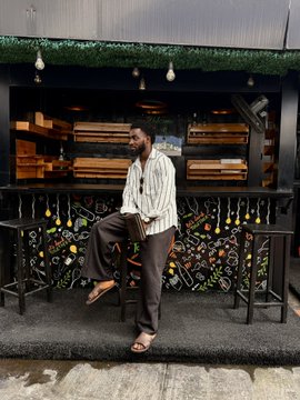 A man sitting on a stool in front of a bar area decorated with a floral mural and dark wooden crates on shelves.