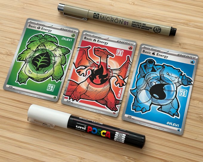Three custom Pokémon Energy cards—Grass (Bulbasaur), Fire (Charmander), and Water (Squirtle)—are displayed on a wooden surface, each labeled "Basic Energy" and signed by artist "0xlevi," accompanied by a Pigma Micron 01 archival ink pen and a Uni Posca marker used to create them.