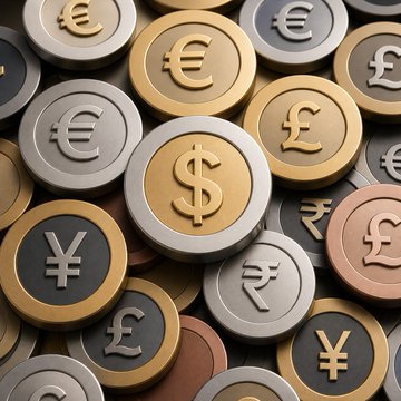 A pile of coins featuring symbols for the euro (€), pound (£), yen (¥), rupee (₹), and a prominently centered dollar ($) coin, representing global currencies. The image visually underscores the article's theme of shifting financial landscapes, where traditional banking's dominance in consumer revenue faces disruption from emerging digital currency solutions like stablecoin wallets.