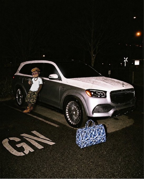 A cartoonish photo composite shows a person with an emoji face wearing a crown, camo shorts, and Timberland boots posing next to a silver Mercedes-Maybach SUV parked at night, with a blue duffel bag nearby.