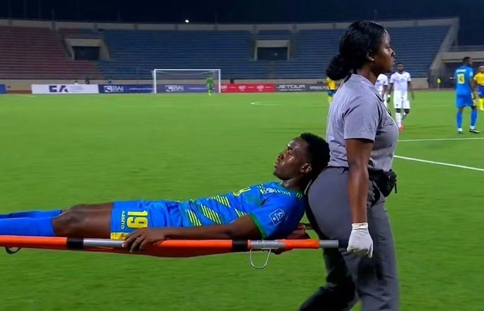 A soccer player wearing a blue and yellow jersey with the number 15 is being carried off the field on a stretcher by a medical staff member in a gray uniform during a night match.