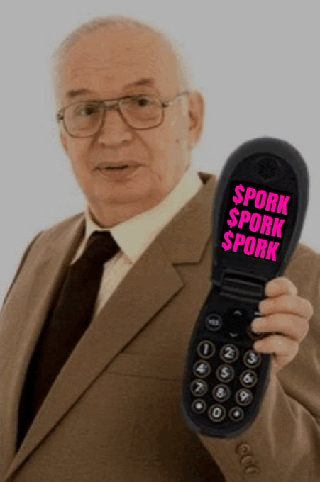 An elderly man in a tan suit and tie holds up a black flip phone displaying the text 'SPORK SPORK SPORK' in pink letters on its screen.
