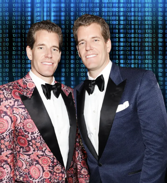 Tyler and Cameron Winklevoss pose in matching tuxedos—one in a striking red and blue paisley pattern and the other in a deep navy—against a digital binary code backdrop, reflecting their deep ties to the cryptocurrency world.