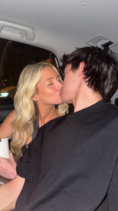 A blonde woman and dark-haired man share a kiss in the backseat of a car. The intimate moment, set against a nighttime backdrop, accompanies a post asking about holdings in $ANSEM, suggesting a casual, personal share tied to crypto culture humor.